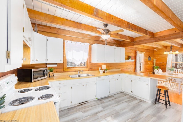 kitchen with range, sink, wood walls, white dishwasher, and beam ceiling