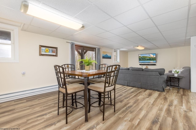 dining area featuring a baseboard heating unit, a drop ceiling, and light hardwood / wood-style flooring