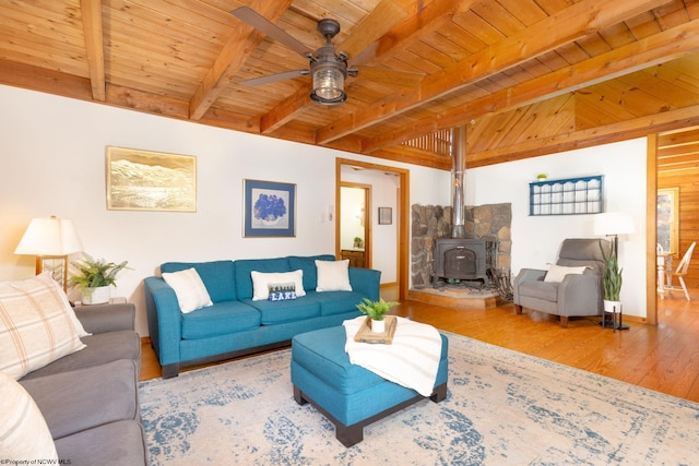 living room featuring a wood stove, light wood-type flooring, ceiling fan, beam ceiling, and wood ceiling