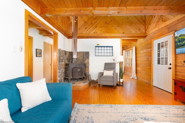 living room with a wood stove, beam ceiling, light hardwood / wood-style floors, and wooden ceiling