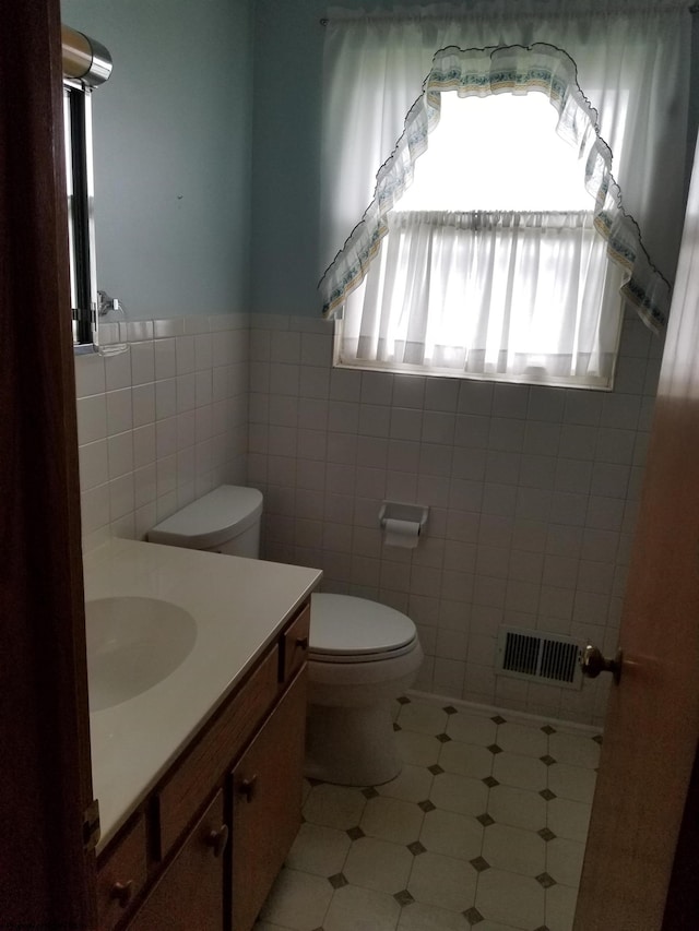 bathroom with tile walls, tile floors, toilet, and vanity