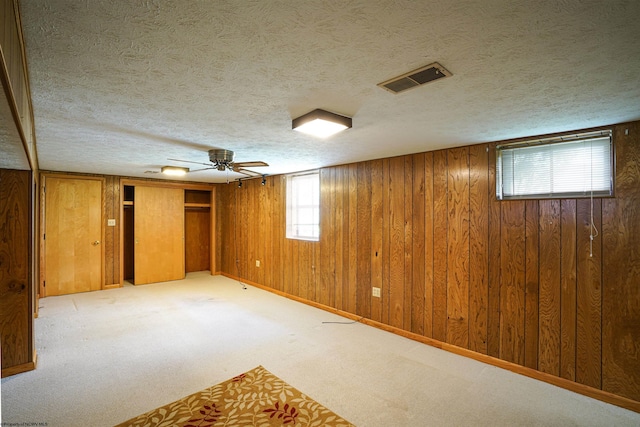 basement featuring ceiling fan, light carpet, wood walls, and a textured ceiling