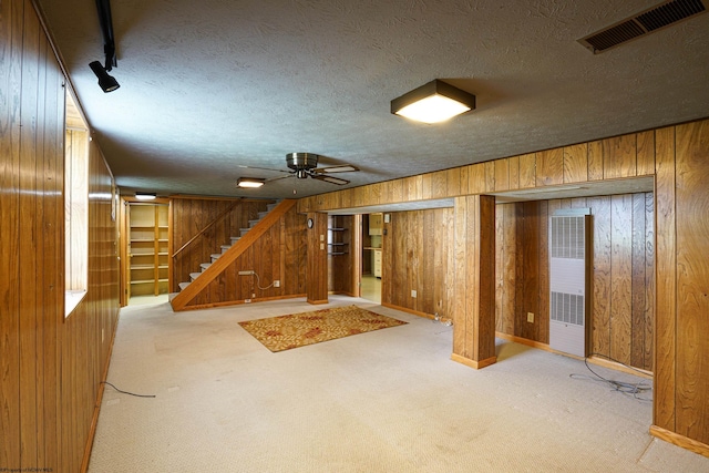 basement with light colored carpet, wood walls, ceiling fan, and a textured ceiling