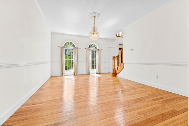 spare room with an inviting chandelier, crown molding, and light hardwood / wood-style flooring