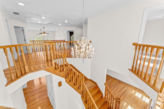 stairway with ceiling fan with notable chandelier and light wood-type flooring