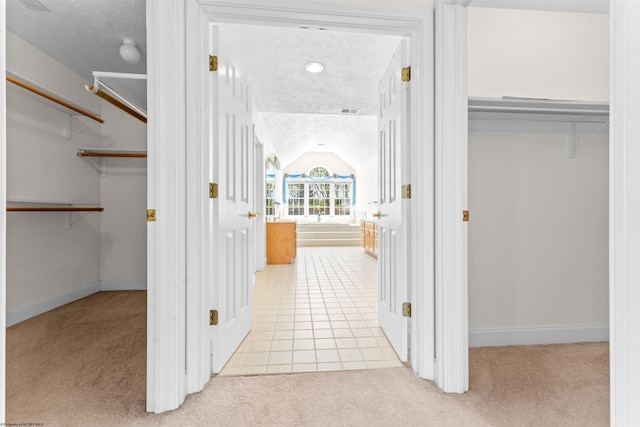 hall with lofted ceiling, a textured ceiling, and light tile flooring