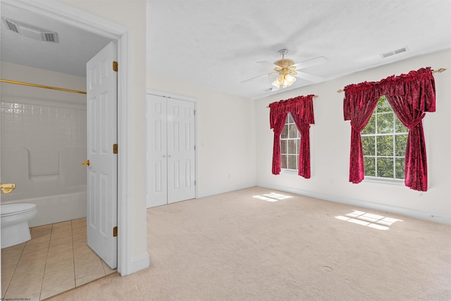 unfurnished bedroom with ceiling fan, light carpet, and connected bathroom