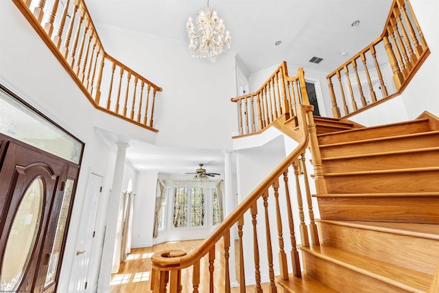 staircase with a notable chandelier, light wood-type flooring, a towering ceiling, and ornamental molding