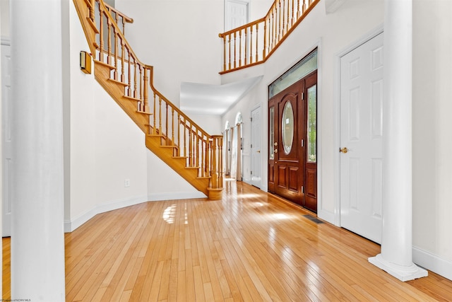 entrance foyer featuring ornate columns, light wood-type flooring, and a towering ceiling