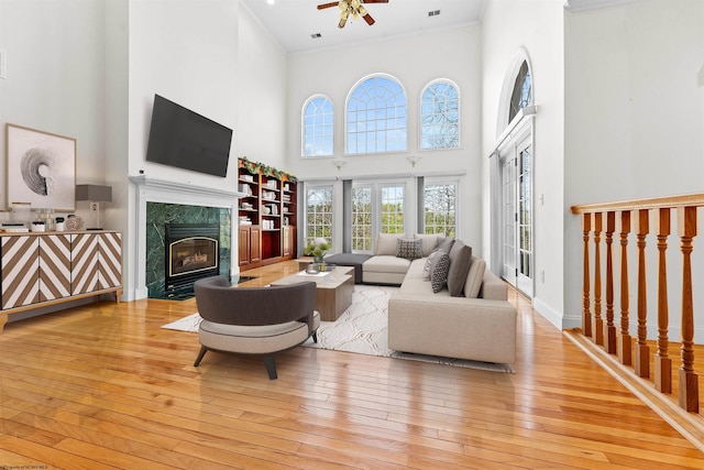 living room featuring light hardwood / wood-style flooring, ceiling fan, a high end fireplace, and a high ceiling