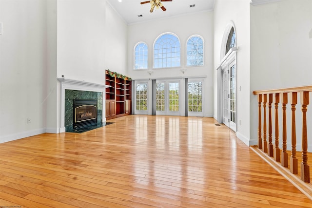 unfurnished living room featuring light wood-type flooring, a fireplace, crown molding, a high ceiling, and ceiling fan