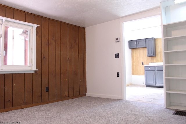 carpeted spare room featuring wooden walls and a textured ceiling