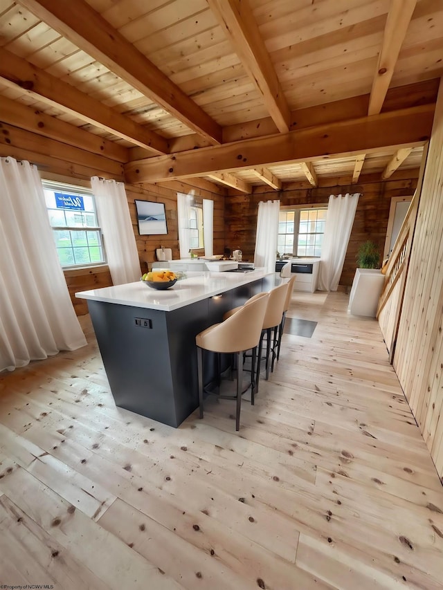 kitchen featuring wooden walls, a healthy amount of sunlight, light hardwood / wood-style flooring, and beamed ceiling