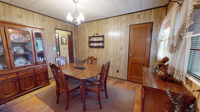 dining room with wood walls, light hardwood / wood-style floors, and a notable chandelier