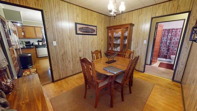 dining space featuring wooden walls, light hardwood / wood-style floors, and a notable chandelier