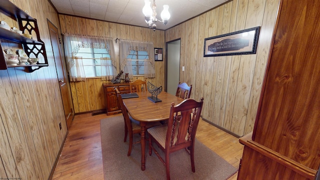 dining space with wooden walls, crown molding, light hardwood / wood-style flooring, and a notable chandelier