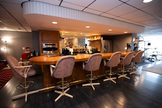 bar with a drop ceiling, appliances with stainless steel finishes, dark wood-type flooring, and sink