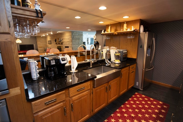 kitchen featuring wood walls, dark hardwood / wood-style floors, sink, stainless steel fridge with ice dispenser, and dark stone counters