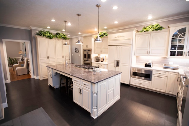 kitchen with appliances with stainless steel finishes, tasteful backsplash, decorative light fixtures, dark hardwood / wood-style floors, and an island with sink