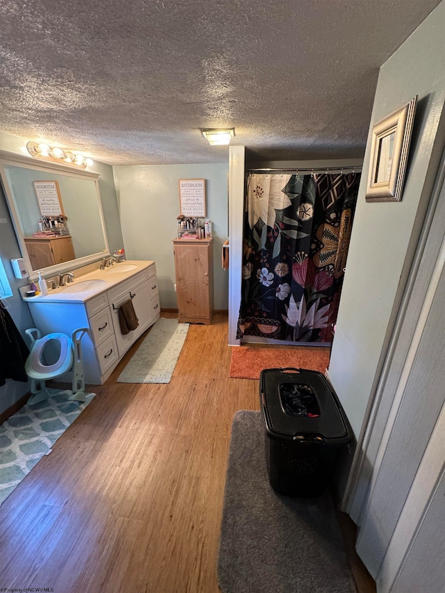 bathroom featuring a sink, double vanity, a textured ceiling, and wood finished floors