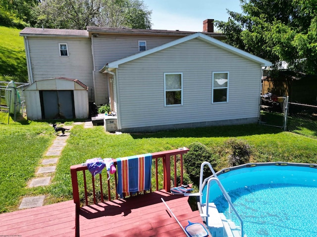 back of property featuring a wooden deck, an outdoor pool, a storage unit, a yard, and an outdoor structure