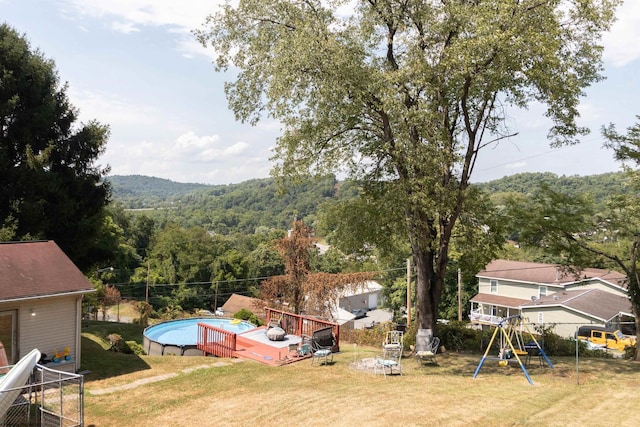 view of yard featuring a deck, a playground, a wooded view, and a fenced in pool