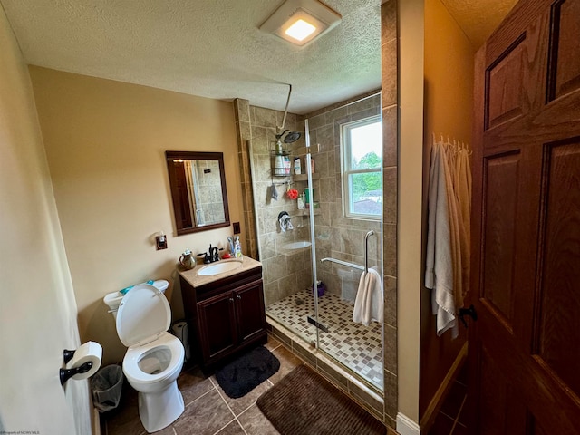 bathroom featuring large vanity, a shower with shower door, tile flooring, toilet, and a textured ceiling