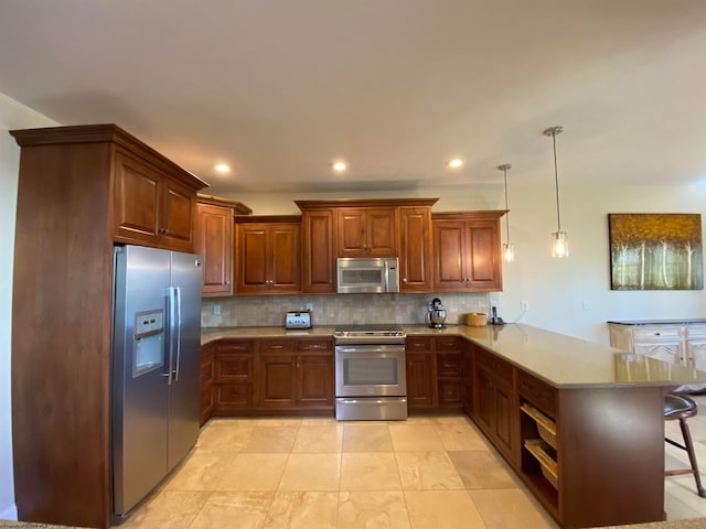 kitchen with appliances with stainless steel finishes, a breakfast bar, tasteful backsplash, hanging light fixtures, and kitchen peninsula