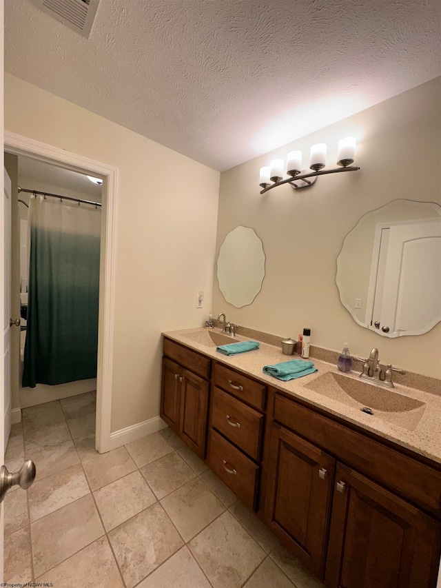 bathroom featuring a textured ceiling, tile floors, and double sink vanity