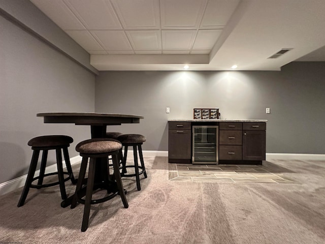 bar featuring wine cooler, light carpet, and dark brown cabinets