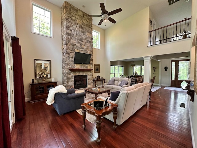 living room featuring ceiling fan, a towering ceiling, a fireplace, dark hardwood / wood-style flooring, and ornate columns