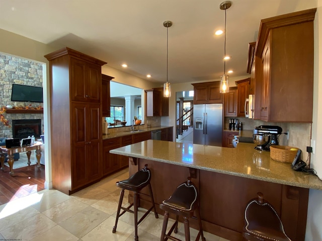 kitchen with backsplash, a stone fireplace, stainless steel appliances, and kitchen peninsula