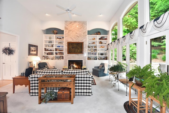 carpeted living room with built in features, ceiling fan, a towering ceiling, and a fireplace