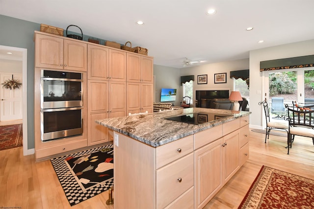 kitchen featuring light brown cabinetry, light hardwood / wood-style flooring, double oven, and a center island