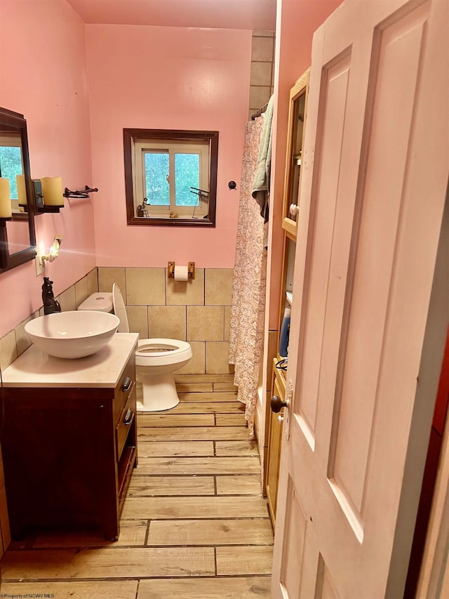 bathroom featuring wood-type flooring, vanity, toilet, and tile walls