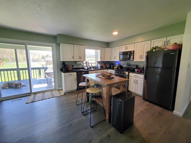 kitchen with black appliances, dark hardwood / wood-style flooring, white cabinets, and a kitchen bar