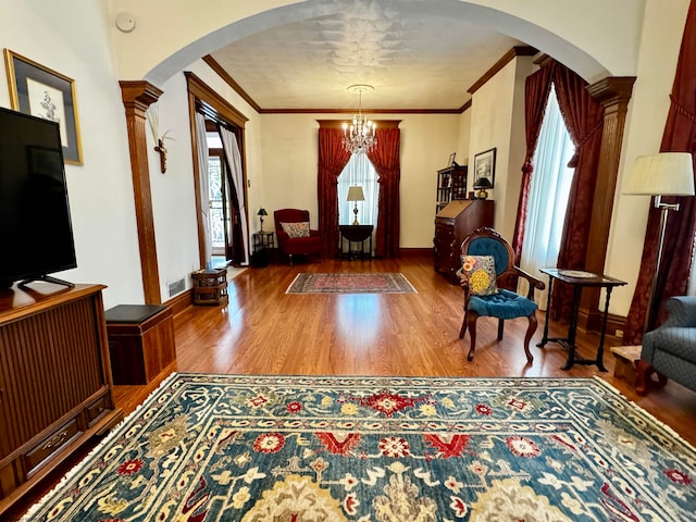 foyer entrance with an inviting chandelier, ornate columns, hardwood / wood-style flooring, and crown molding