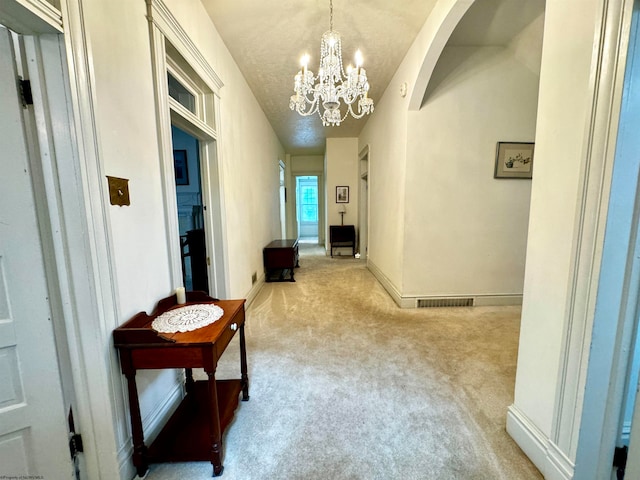 corridor featuring a textured ceiling, carpet, and an inviting chandelier