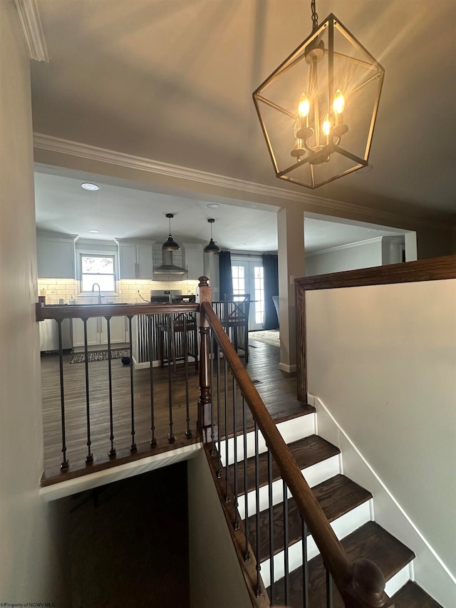 staircase featuring plenty of natural light, crown molding, and a notable chandelier