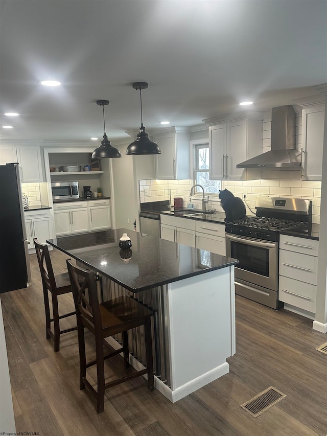 kitchen featuring appliances with stainless steel finishes, wall chimney range hood, a center island, and dark hardwood / wood-style flooring