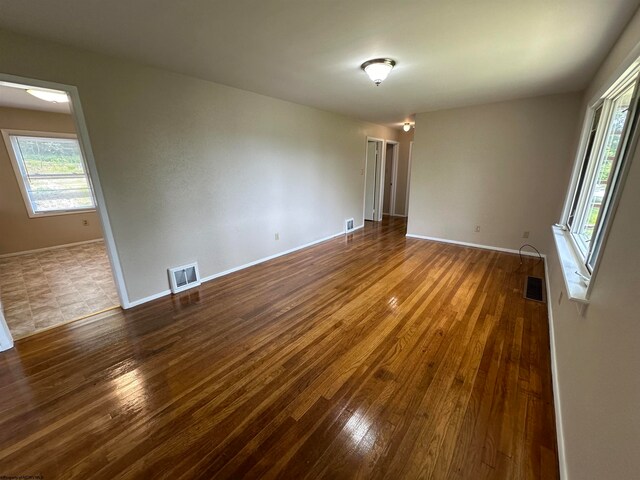 unfurnished room featuring wood-type flooring, visible vents, and baseboards