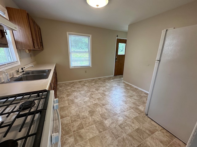 kitchen featuring custom exhaust hood, white refrigerator, light tile patterned floors, stainless steel gas stove, and sink