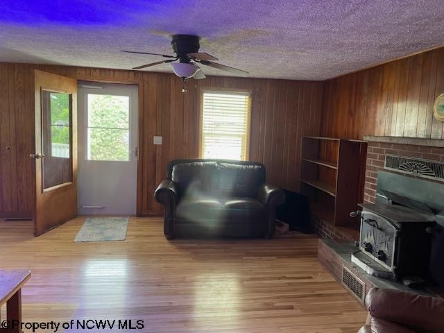 living room featuring wooden walls, light hardwood / wood-style floors, a textured ceiling, and a wood stove