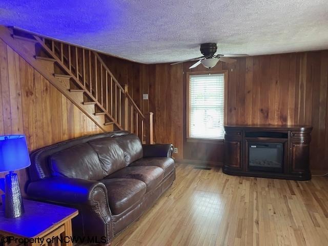 living room with ceiling fan, light wood-type flooring, a textured ceiling, and wooden walls