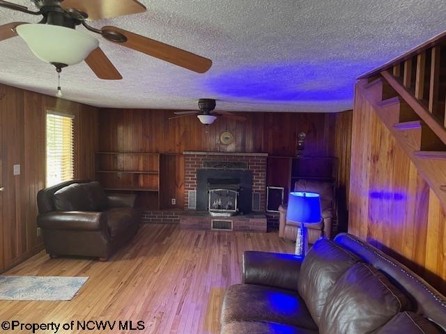 living room with ceiling fan, light wood-type flooring, a textured ceiling, and wood walls