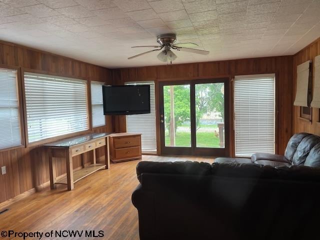 living room featuring light hardwood / wood-style floors, ceiling fan, and wood walls