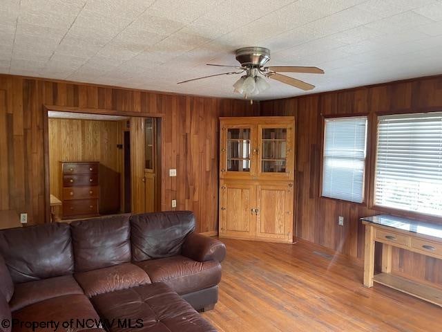 living room with ceiling fan, wood-type flooring, and wood walls