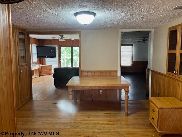 dining space featuring hardwood / wood-style flooring, wooden walls, a textured ceiling, and ceiling fan