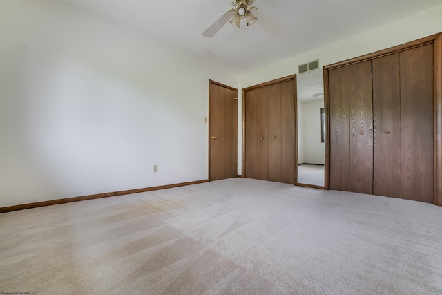 unfurnished bedroom with multiple closets, light carpet, and ceiling fan