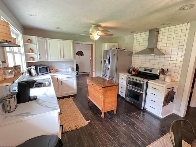 kitchen featuring ceiling fan, backsplash, wall chimney exhaust hood, white cabinets, and appliances with stainless steel finishes